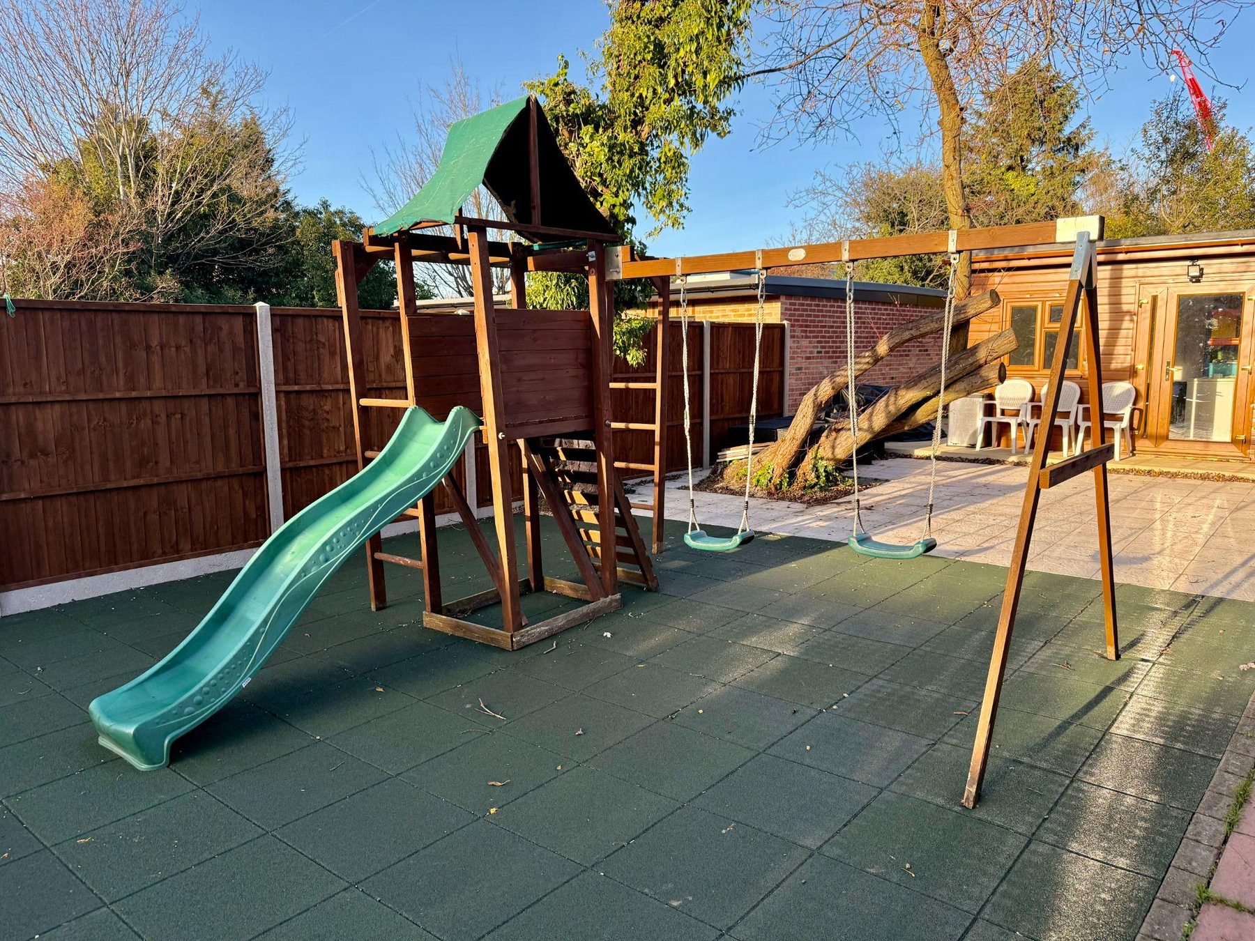Garden play area with wooden climbing frame, slide and swings