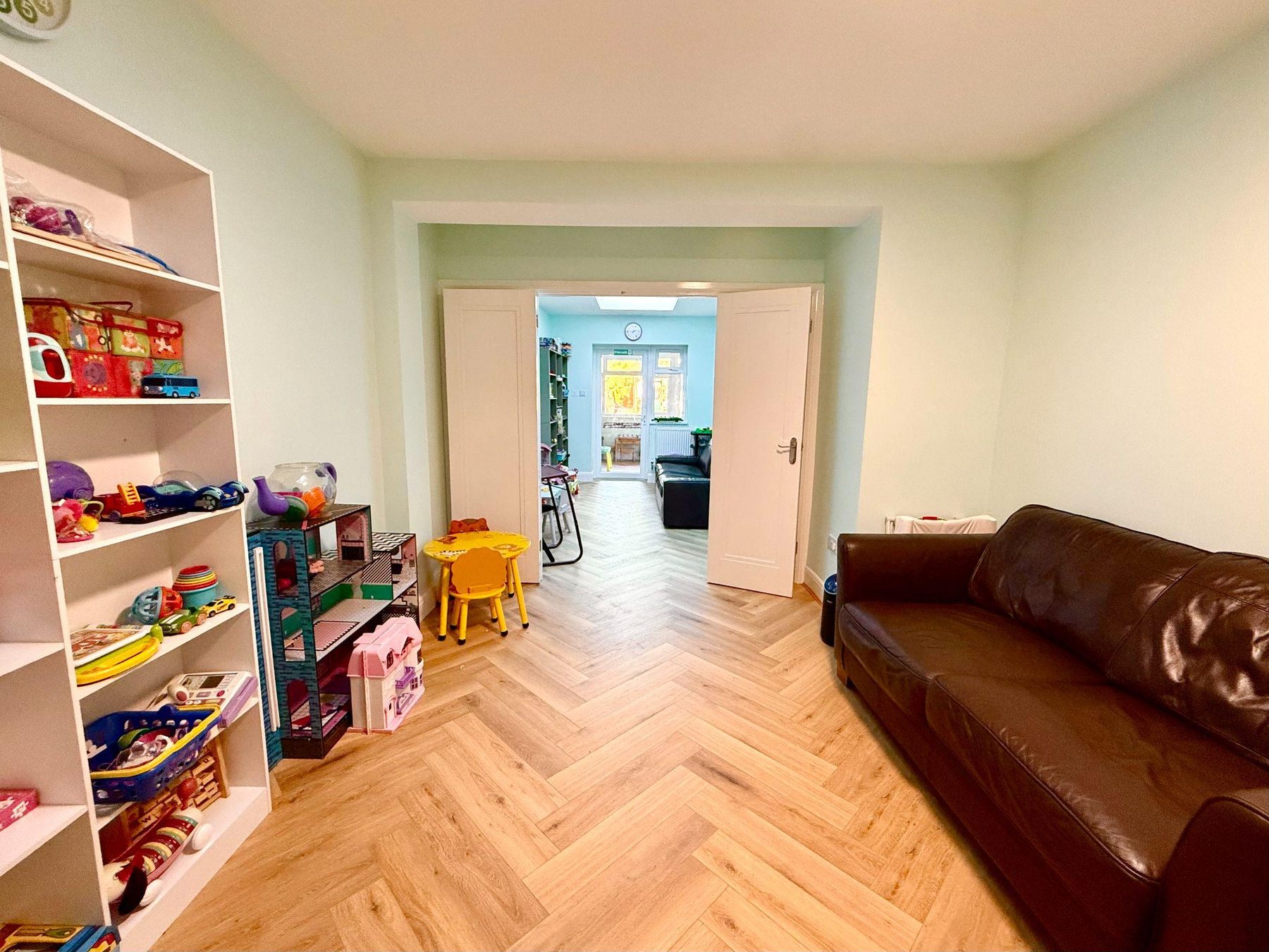 Family room with sofa and toy shelves opening into a second room