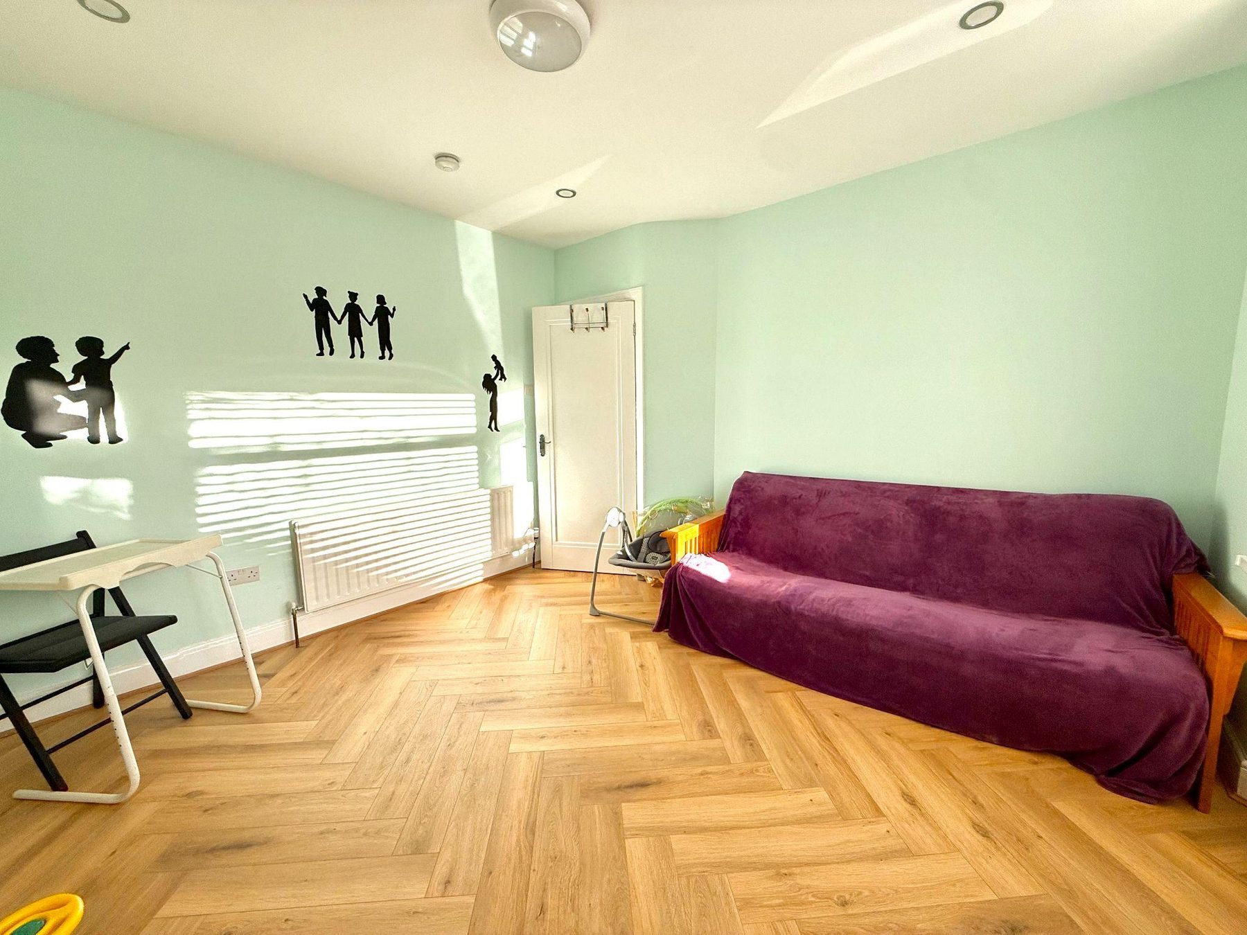 Green room with purple sofa, small table and window blinds
