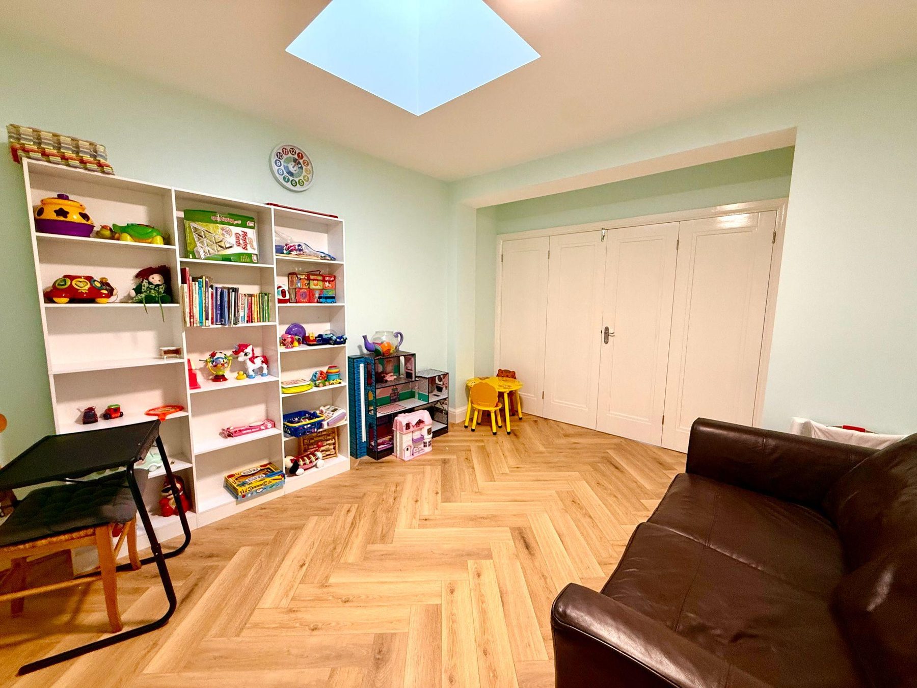 Room with bookshelves, children's table and leather sofa under a skylight