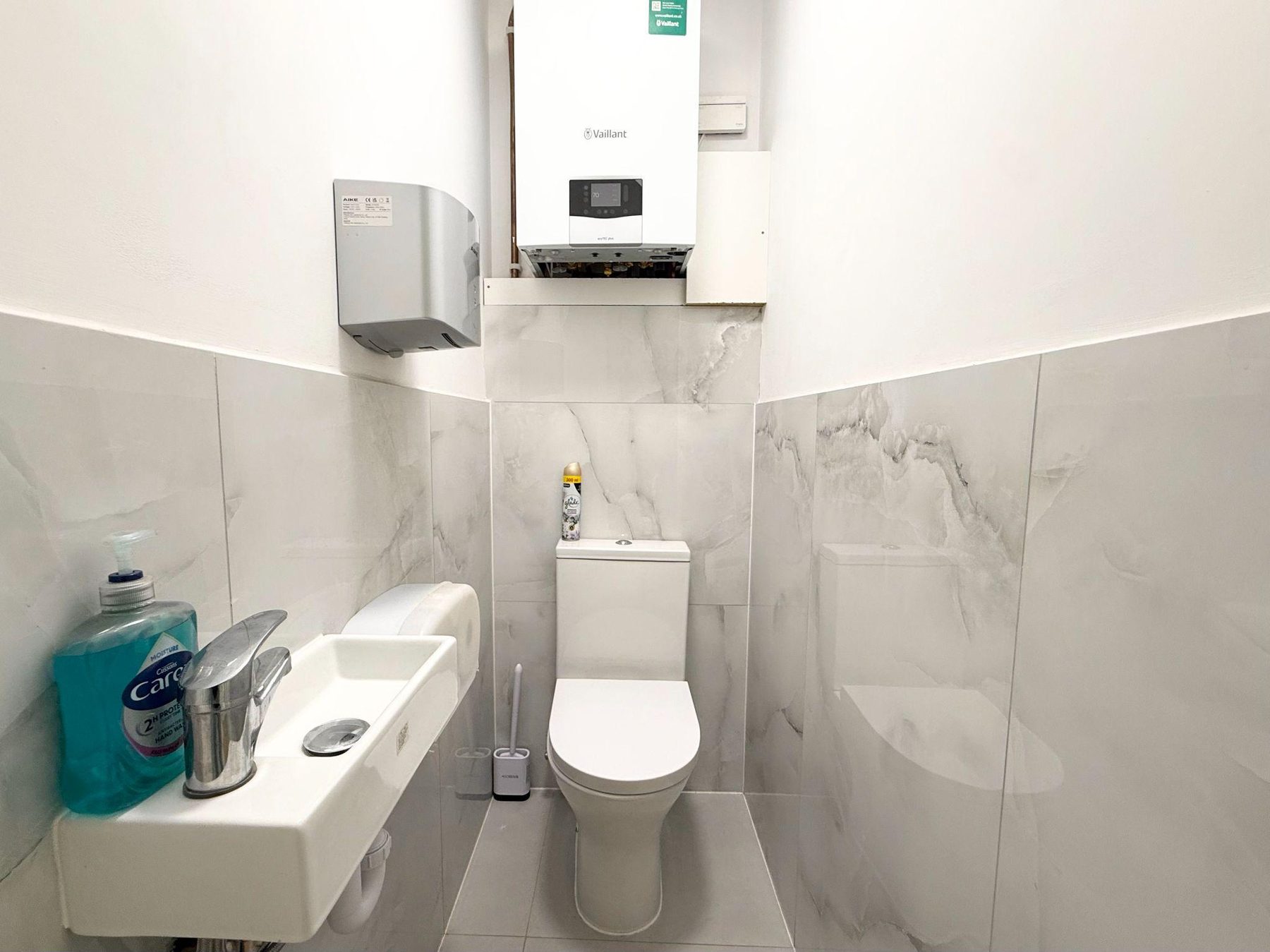 Small tiled cloakroom with toilet, basin and hand towel dispenser
