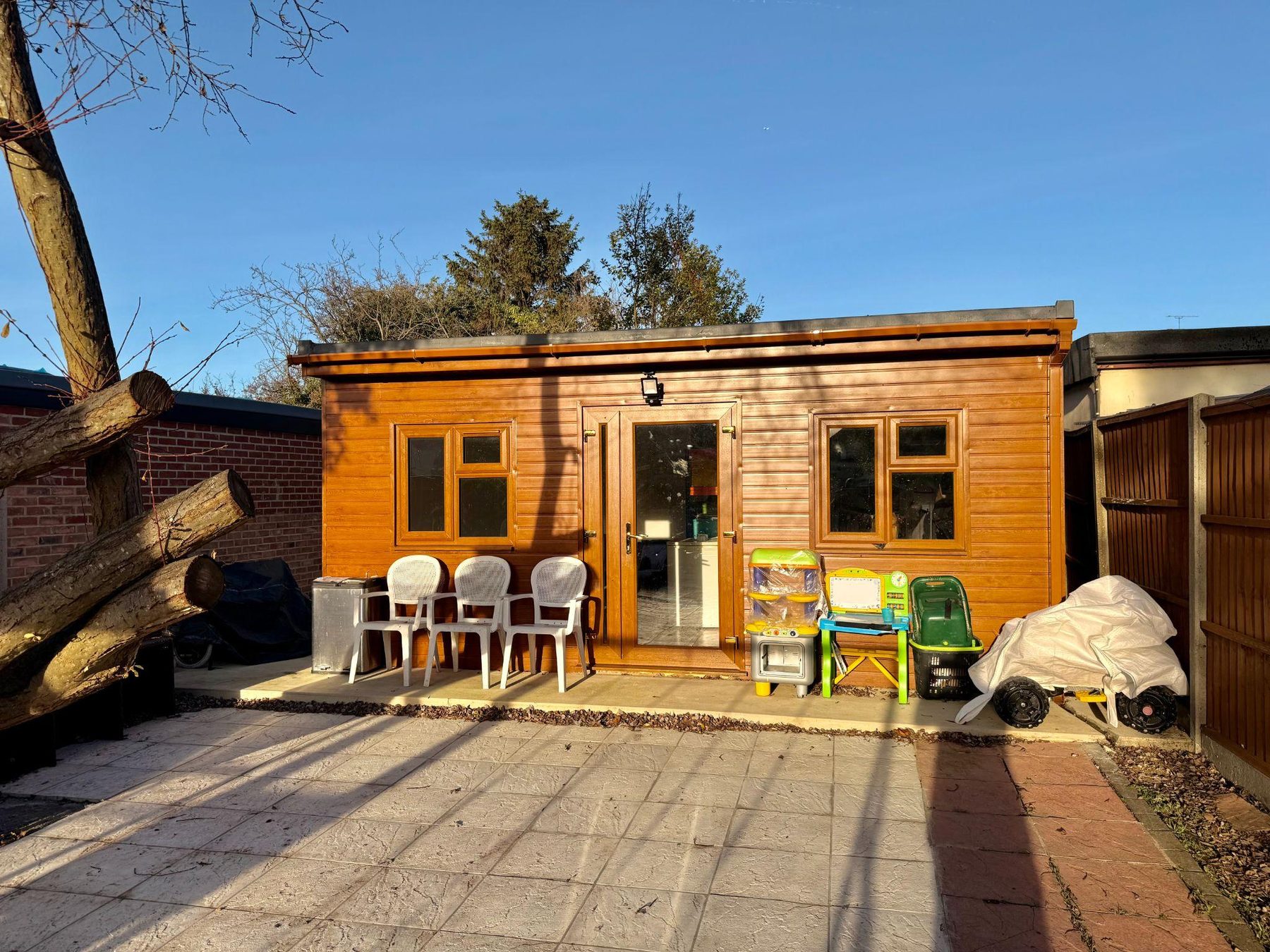 Timber garden cabin with chairs and children's ride-on toys outside